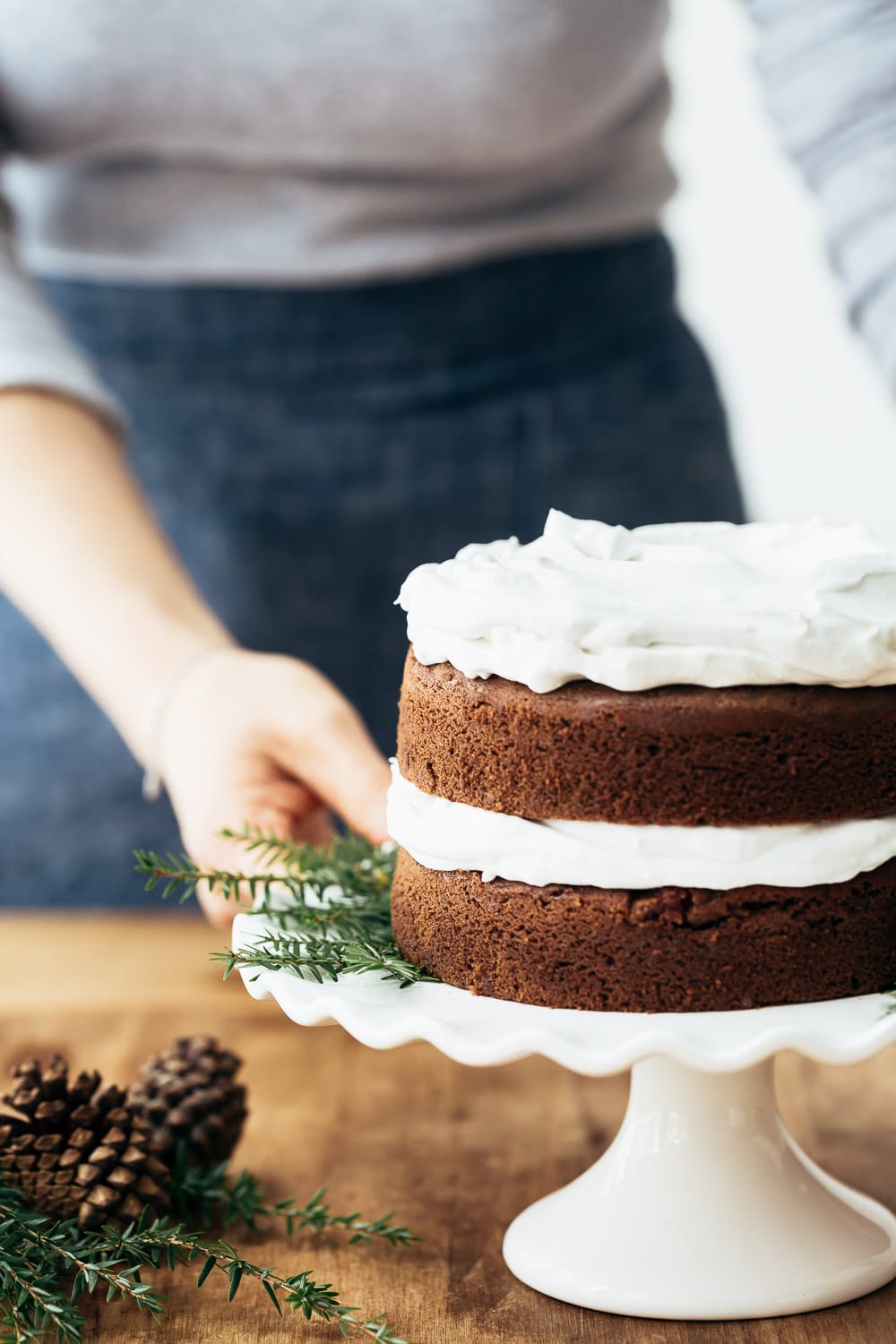 A woman is photographed from the front view as she is getting ready to garnish a Coconut Flour Gingerbread Cake with cranberry topping.