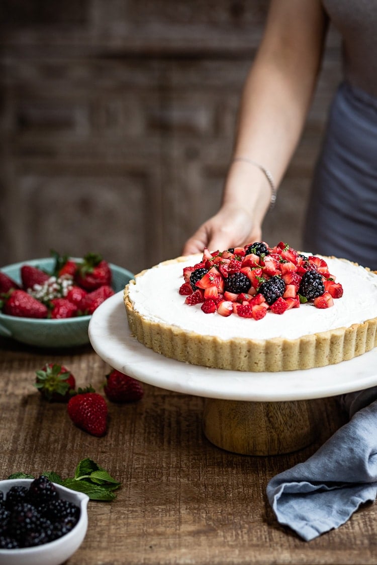 An almond flour baked good, Strawberry Tart, is topped off with berries served by a woman.